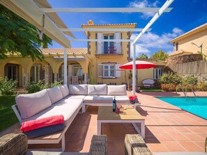 A poolside area with a sofa, a table, and a red umbrella.