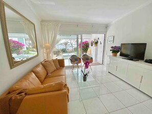 Uma sala de estar com sofá, televisão e mesa de centro de vidro.