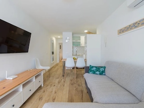 Una sala de estar moderna con televisor de pantalla plana, un escritorio de madera, un sofá y un comedor con sillas.