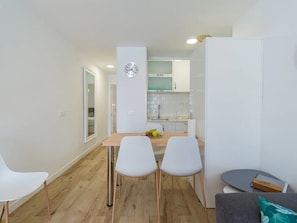Una cocina moderna con armarios blancos, un reloj y un comedor con dos sillas blancas y una mesa.