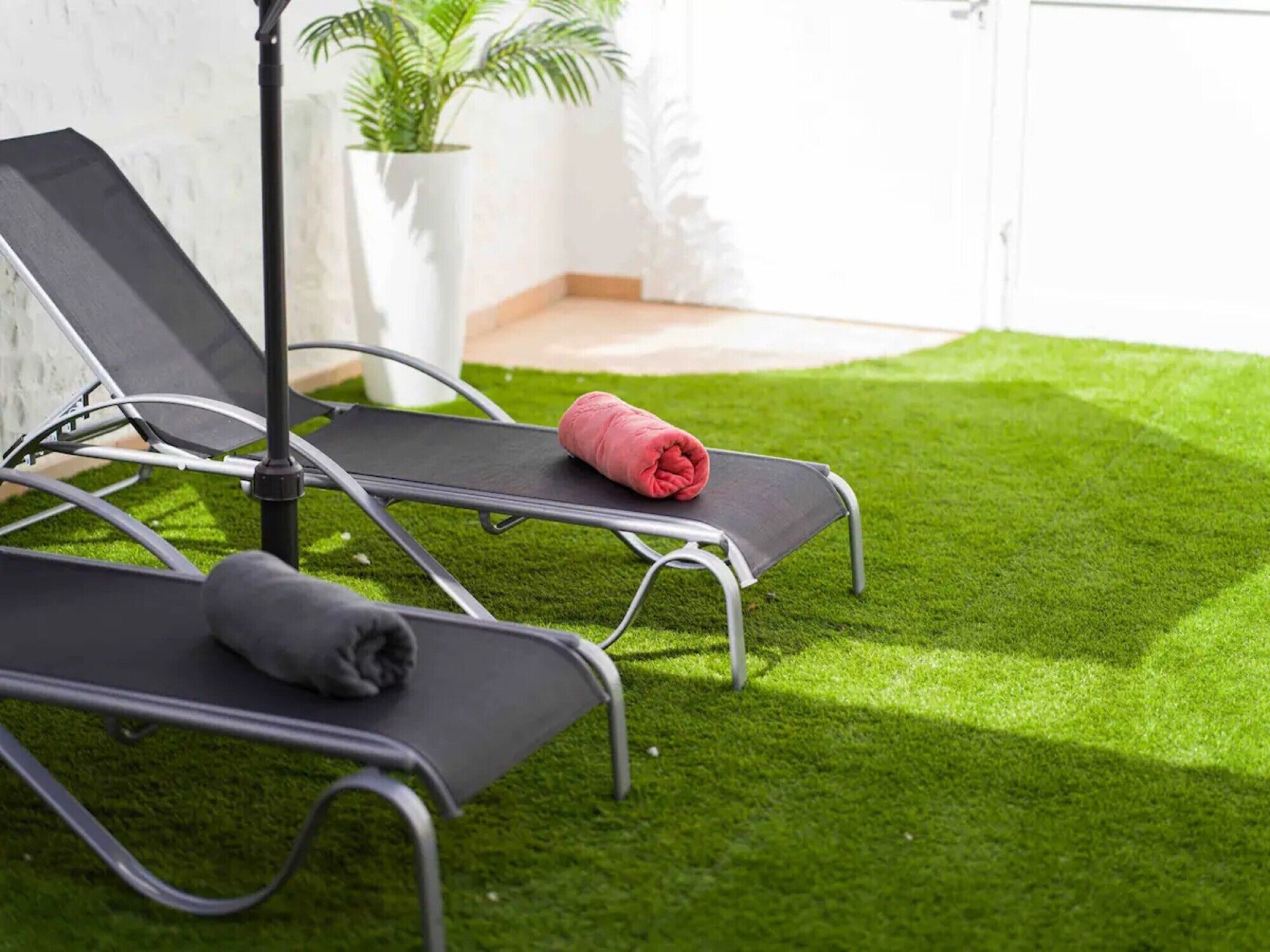 Two reclining chairs on artificial grass, a potted plant, and a white wall.