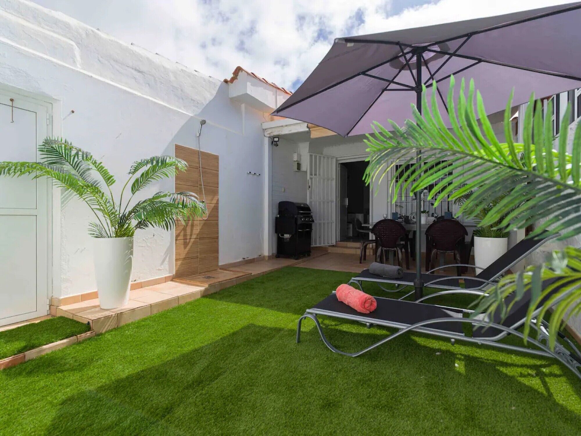 A patio with a grill, outdoor seating, and potted plants.