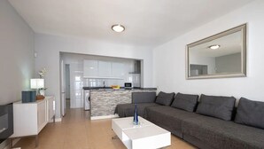 A modern living room with a grey sofa, a white coffee table, and a kitchen in the background.