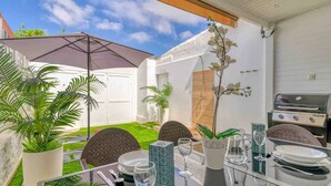 An outdoor dining area with a table set for four, surrounded by chairs, a grill, and potted plants.
