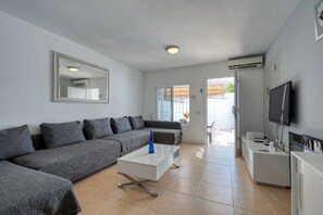 A modern living room with a grey sofa, a white coffee table, a TV, and an air conditioning unit.