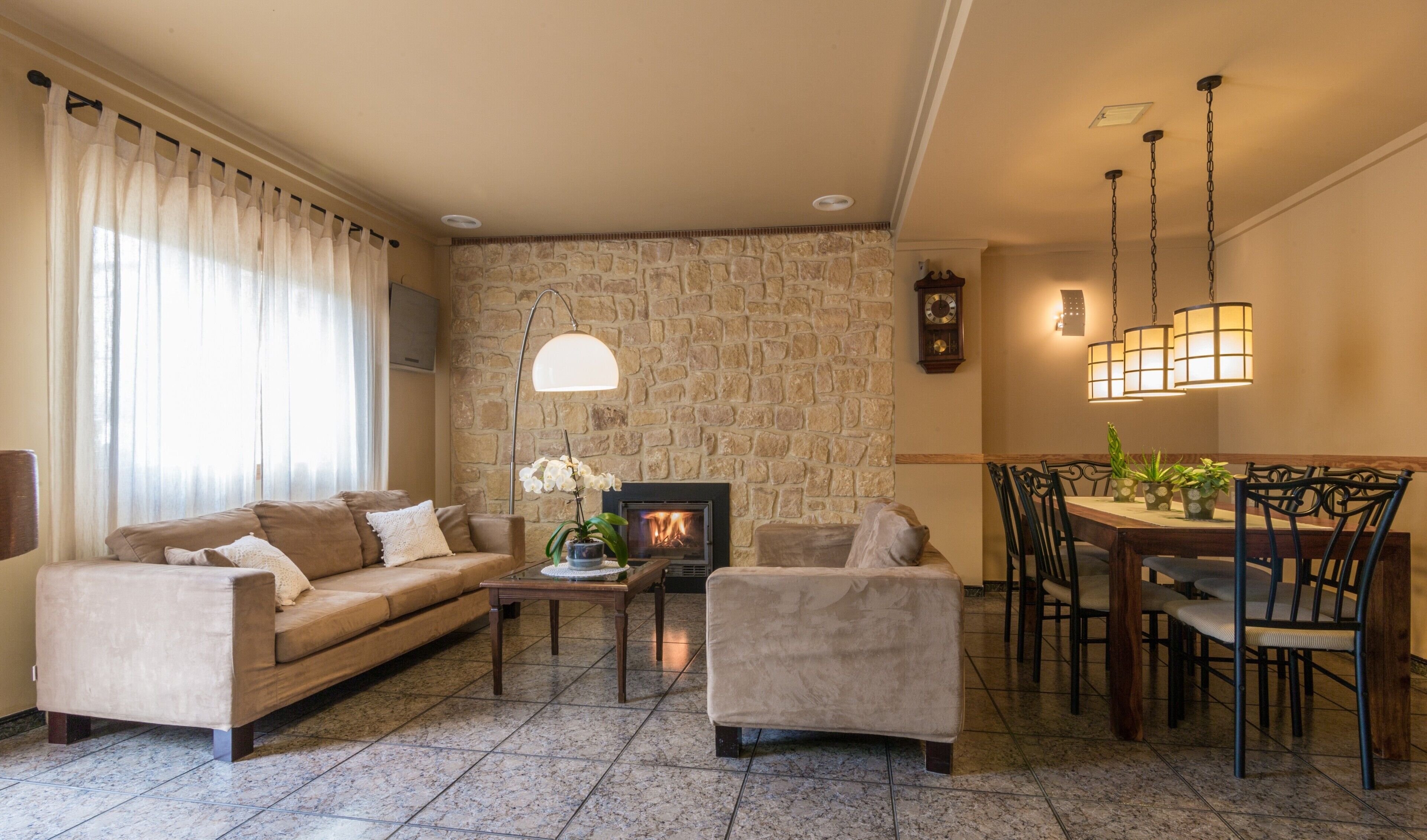 Un salon avec un mur en pierre, une cheminée, un coin repas avec des chaises et un canapé.