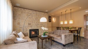 A living room with a stone wall, a fireplace, a dining area with chairs, and a table.