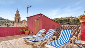 A rooftop terrace with two sun loungers, a small red building, and a church in the background.