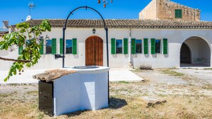 Un edificio con techo de tejas, puerta de madera central y contraventanas verdes.