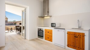 Cocina compacta equipada con microondas, horno y lavavajillas, armarios de madera y vistas a un patio exterior.