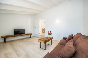 Un soggiorno moderno con TV a schermo piatto, panchetta in legno, tavolino da caffè, divano marrone e una pianta in vaso con fiori rossi.
