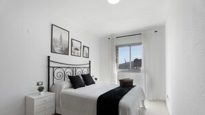 Ein Schlafzimmer mit einem Bett, einem Nachttisch, einem Fenster mit Vorhängen und gerahmten Bildern an der Wand.