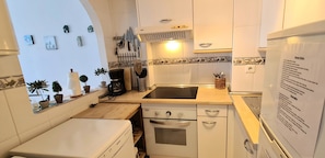 Een kleine keuken met witte apparaten, een inbouwoven, een vaatwasser en een spoelbak.
