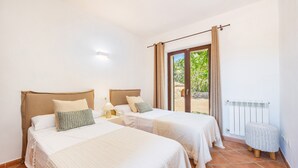 A bedroom with two beds, a window with curtains, a radiator, and a small stool. - Holiday Home 'Na Berganta' with Private Terrace, Private Garden and Wi-Fi (Illes Balears)