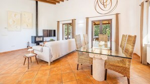 A living room with a glass table, wicker chairs, a sofa, a TV, and artwork on the wall. - Holiday Home 'Na Berganta' with Private Terrace, Private Garden and Wi-Fi (Illes Balears)