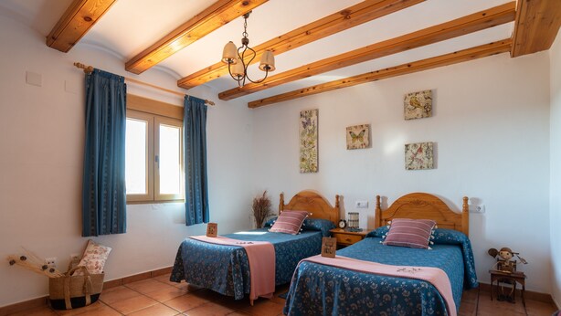 A bedroom with two beds, wooden beams, a chandelier, and artwork on the walls. - Apartment 'Torre Amador' with Mountain View, Private Pool and Private Terrace (Culla)