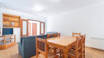 A dining area with a wooden table and chairs, a blue sofa, and a television on a wooden stand.