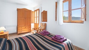 A bedroom with a bed, wooden wardrobe, chair, and a window with a view.