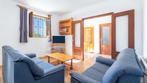 A living room with a TV, sofas, a wooden coffee table, and a window with curtains.