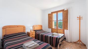 Una camera da letto con due letti, una finestra con tende, un appendiabiti in legno e un comodino con una lampada.