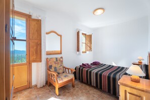 A room with a bed, a chair, a wooden cabinet, a window with curtains, and a view of the outdoors. - Holiday Home 'Casa Del Practicant' with Mountain Views, Private Terrace and Private Garden (Culla)