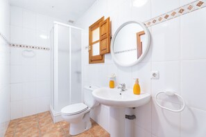 A bathroom with a toilet, sink, mirror, and shower.