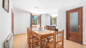 A dining area with a wooden table and chairs, a radiator, and a door with a frosted glass panel. - Apartment 'Antiga Escola De Molinell' with Mountain View, Private Terrace and Private Garden (Culla)