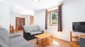A living room with a sofa, a coffee table, a TV, and a window with curtains. - Apartment 'Antiga Escola De Molinell' with Mountain View, Private Terrace and Private Garden (Culla)