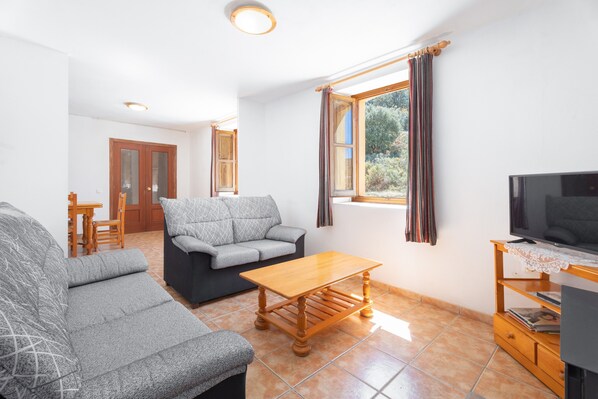 A living room with a sofa, a coffee table, a TV, and a window with curtains.