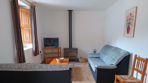 A living room with a sofa, a television, a fireplace, and a wooden chair. - Apartment 'Antiga Escola De Molinell' with Mountain View, Private Terrace and Private Garden (Culla)