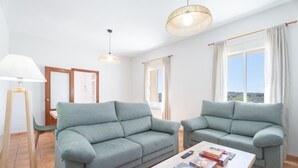 Un salon avec deux canapés, une table basse, une lampe et une fenêtre avec des rideaux.