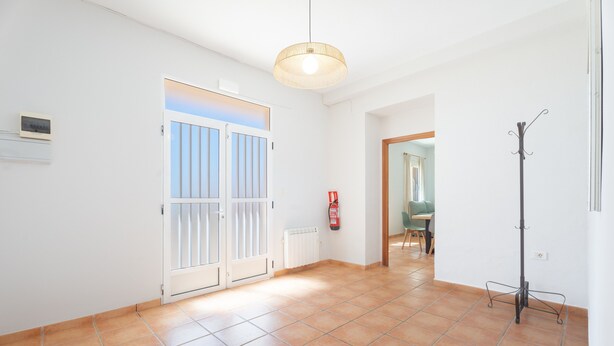 Une pièce spacieuse avec un sol carrelé, une porte donnant sur une vue agréable, un luminaire suspendu et un porte-manteau.