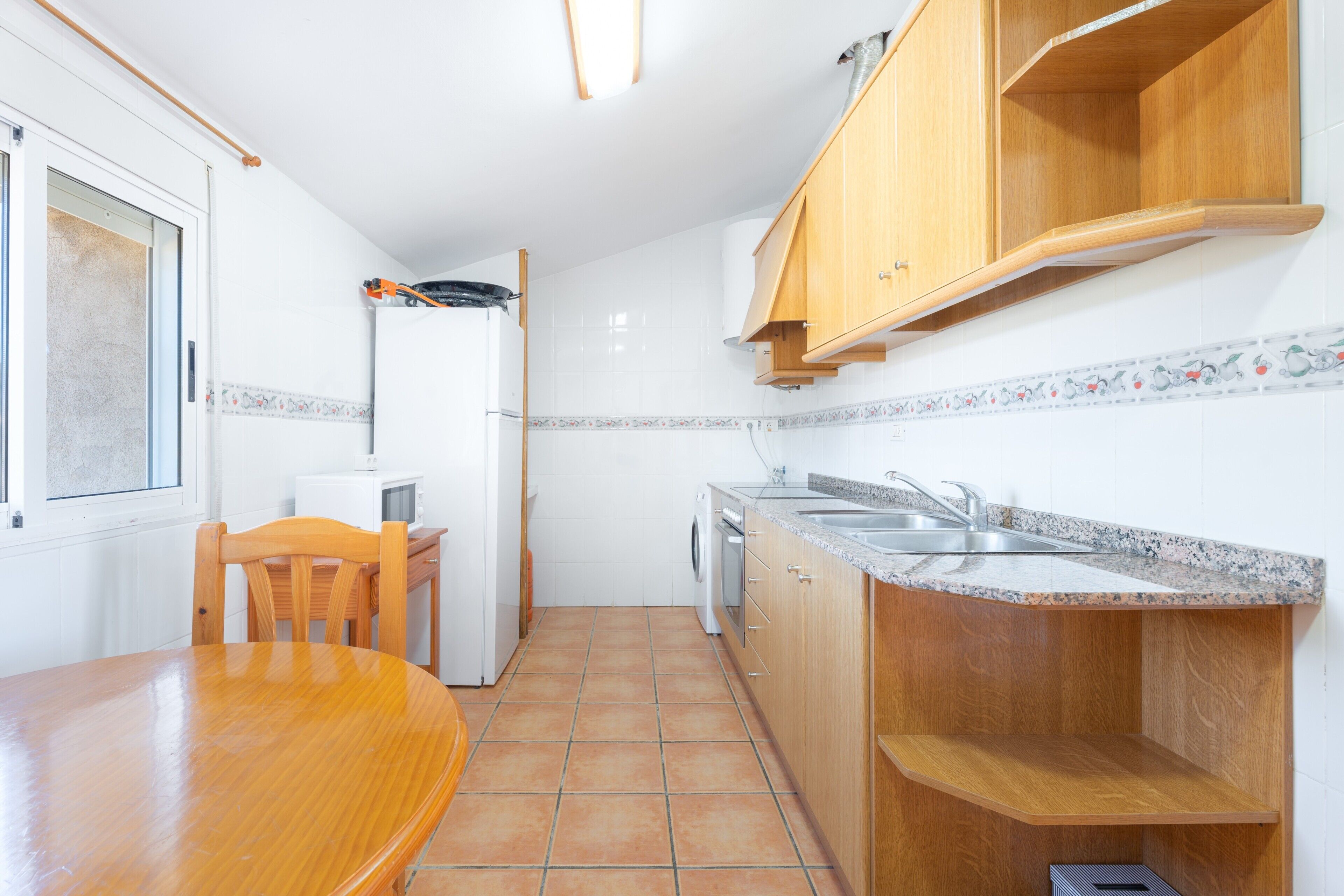Una cocina compacta con una mesa de comedor, armarios de madera, lavadora y ventana.