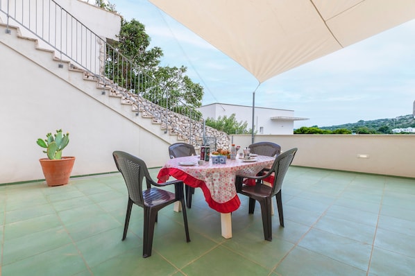 Un comedor con una mesa preparada para cuatro personas, rodeada de sillas, un cactus en maceta y una escalera que sube a un nivel superior.