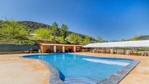 A swimming pool with a curved edge, a covered seating area, and a building with a door and windows in the background. - Caravan 'Bungalow 2' with Mountain View, Wi-Fi and Air Conditioning (Alós de Balaguer)