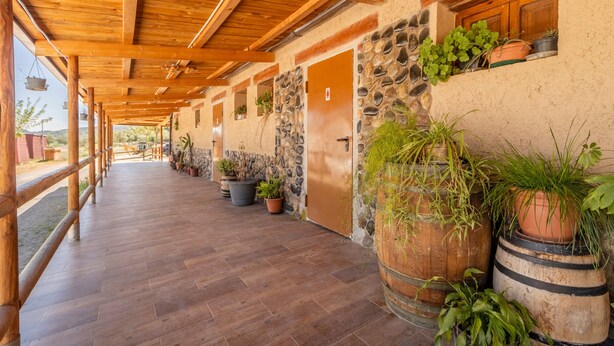 A covered corridor with wooden beams, stone walls, and potted plants. - Caravan 'Bungalow 2' with Mountain View, Wi-Fi and Air Conditioning (Alós de Balaguer)
