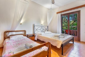 A bedroom with two wooden beds, a nightstand, a bedside table, a window with a view of greenery, and a door leading outside.