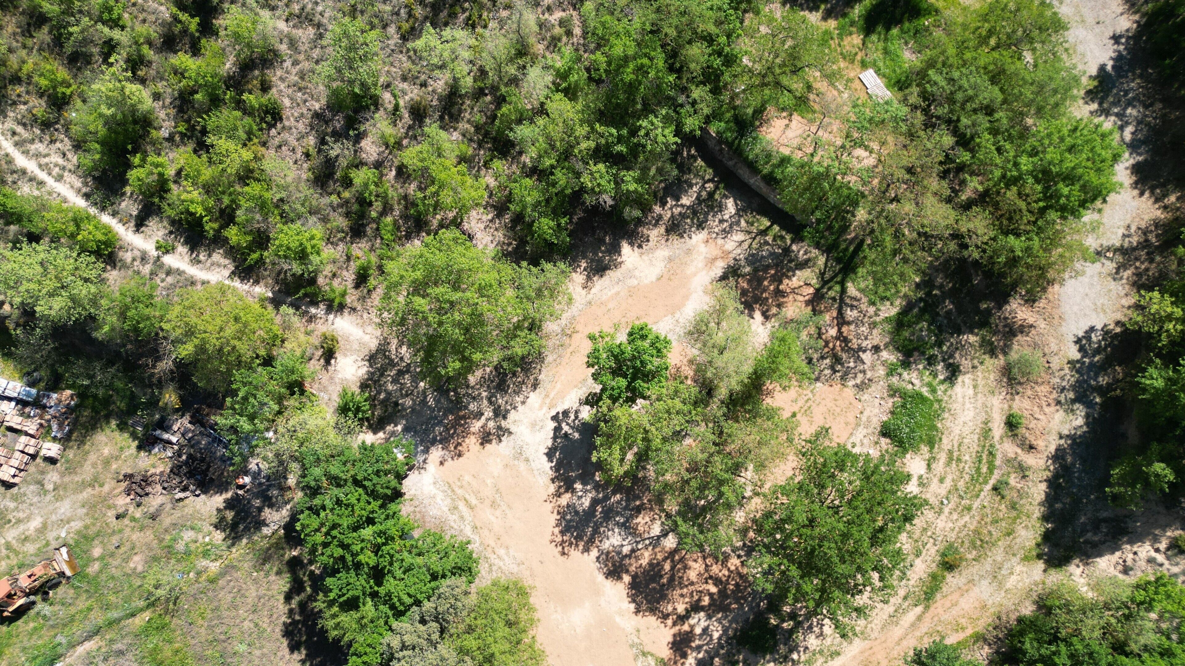 Vista aérea de una zona boscosa con un sendero de tierra y algunos equipos de construcción.