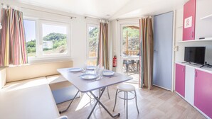 A bright room with a dining table, chairs, a bench, a TV, and a view of greenery outside.