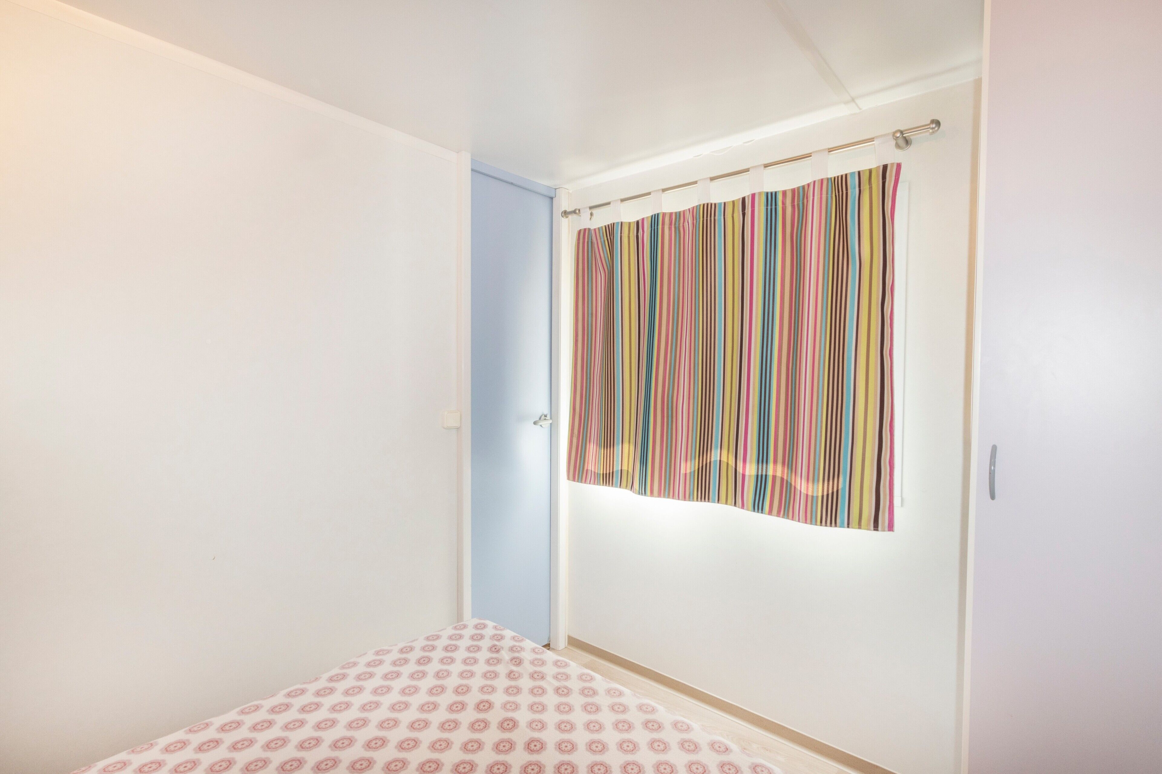 Una habitación con cama, una puerta y una ventana con cortina a rayas.