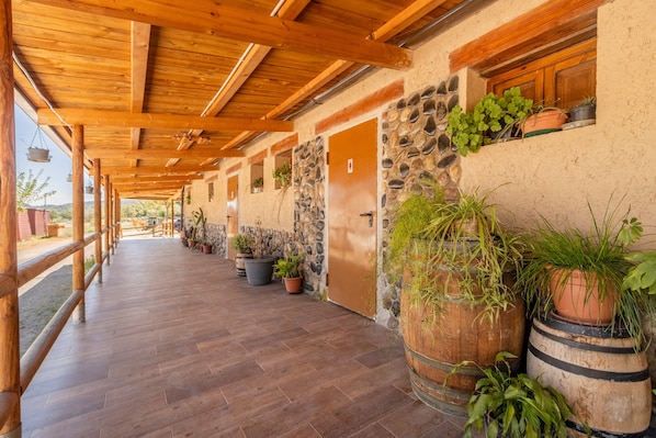 A covered corridor with wooden beams, stone walls, and potted plants.