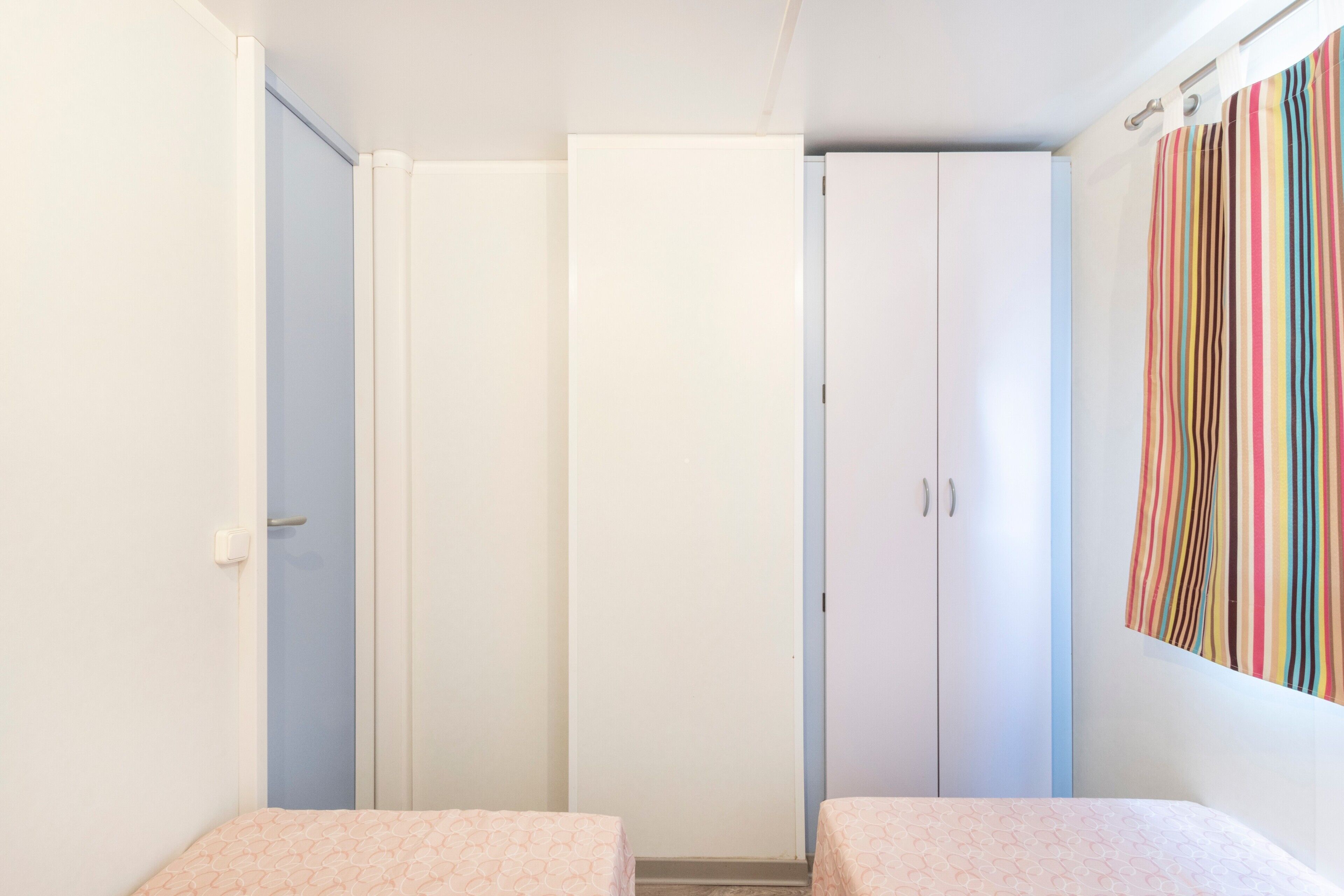 Una habitación con dos camas, un armario y una cortina a rayas.