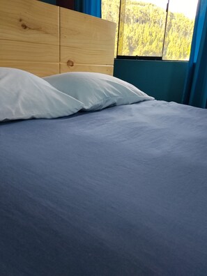Een bed met een houten hoofdbord, witte kussens en een blauwe deken.