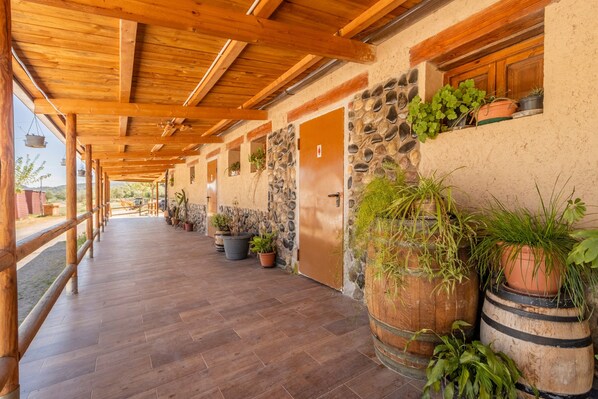 A covered corridor with wooden beams, stone walls, and potted plants.