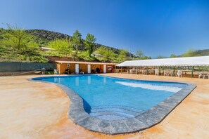 A swimming pool with a curved edge, a covered seating area, and a building with a door and windows.