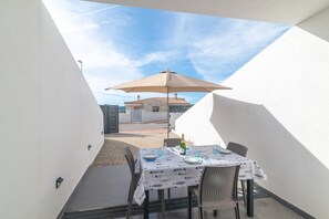 A dining area with a table set for two, an umbrella, and a view of a building in the background.