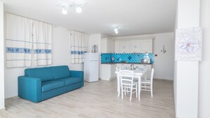 Una cocina moderna con armarios blancos, un salpicadero de azulejos azules y una zona de comedor con sillas y mesa blancos.