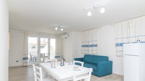 Una habitación moderna y bien iluminada con una mesa de comedor, sillas, un sofá azul y un refrigerador blanco.