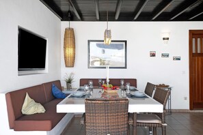 Un coin repas avec une table blanche, des chaises en osier, un canapé marron et un grand tableau encadré au mur.