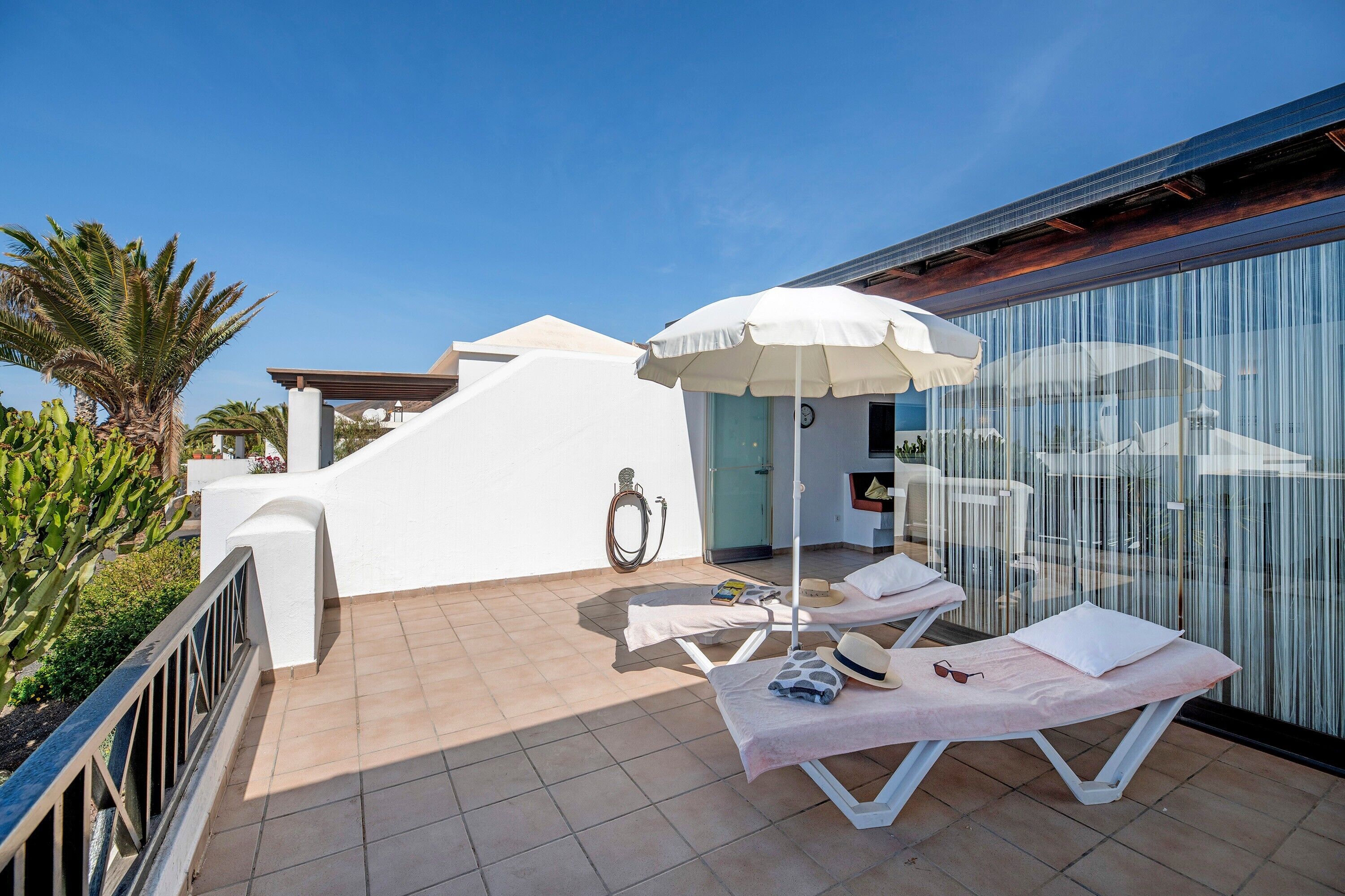 Un balcon avec deux chaises longues, un parasol blanc et une porte vitrée donnant sur une pièce.